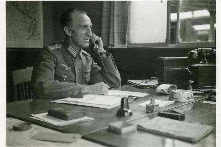 Een Duits officier in een Belgisch kantoor in het station van Bergen. De Wehrmacht Verkehrs Direktion neemt grote delen van het strategisch en operationeel bedrijfsbeheer van de NMBS op agressieve manier over. Bron: privéverzameling Paul Pastiels. Een Duits officier in een Belgisch kantoor in het station van Bergen. De Wehrmacht Verkehrs Direktion neemt grote delen van het strategisch en operationeel bedrijfsbeheer van de NMBS op agressieve manier over. Bron: privéverzameling Paul Pastiels.